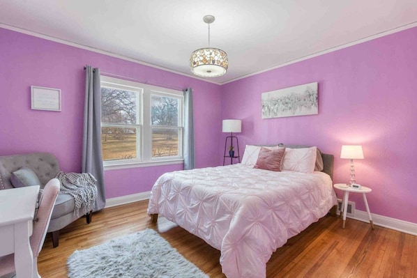A bedroom with a bed, a desk, a chair, a window, and a lamp.