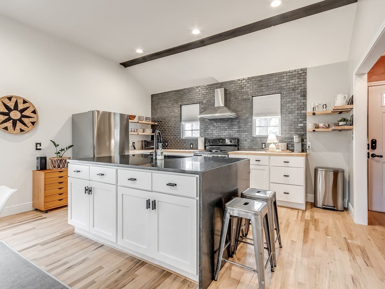A modern kitchen with a central island, stainless steel appliances, and a brick backsplash.