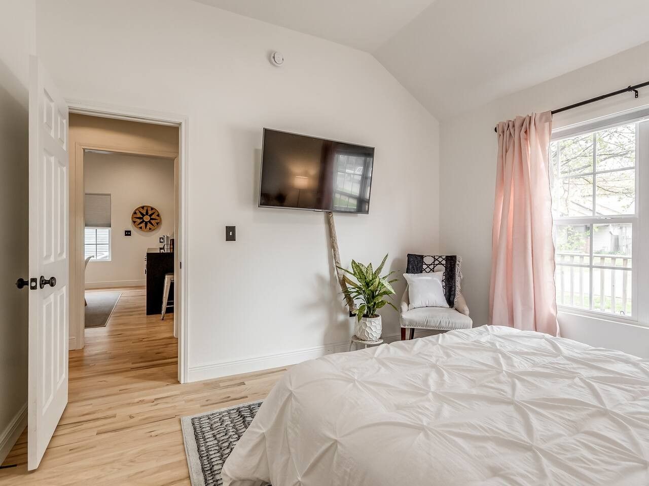 A bedroom with a bed, a TV mounted on the wall, a chair, and a window with curtains.