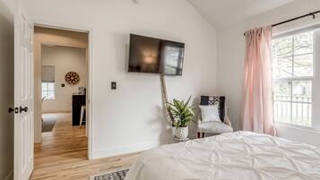 A bedroom with a bed, a TV mounted on the wall, a chair, and a window with curtains.