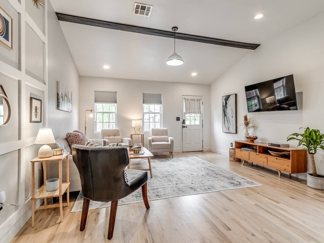 A spacious living room with a modern design, featuring a black leather chair, a wooden coffee table, and a large TV mounted on the wall.