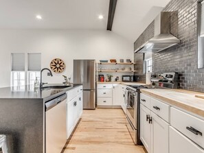 Une cuisine moderne dotée d’appareils électroménagers en acier inoxydable, d’un plancher en bois et d’un mur de fond en briques.