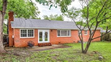 A single-story brick house with a front porch, a chimney, and a tree in the yard.
