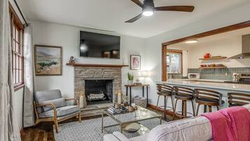 A living room with a fireplace, a ceiling fan, and a kitchen area with bar stools.
