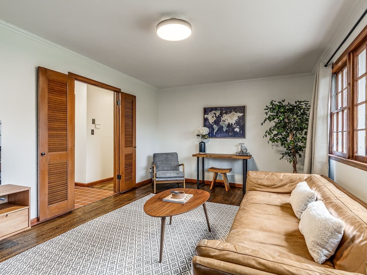 Una sala de estar con sofá, mesa de centro, sillón, escritorio y una planta.