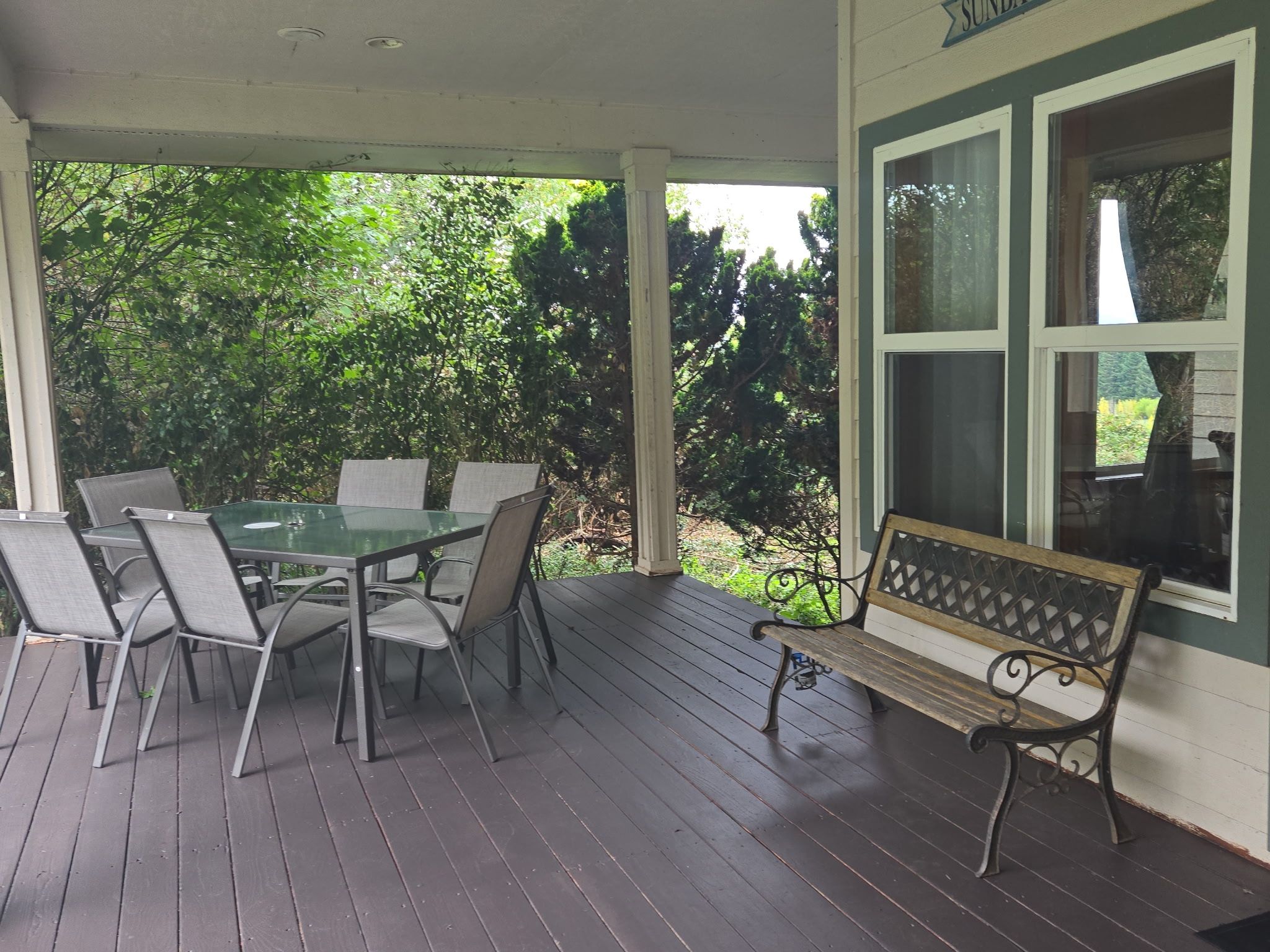 A covered porch with a table and chairs, a bench, and a window.