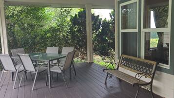 A covered porch with a table and chairs, a bench, and a window.