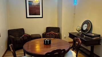 Een eetgedeelte met een ronde tafel, stoelen, een klok en een ingelijst schilderij aan de muur.