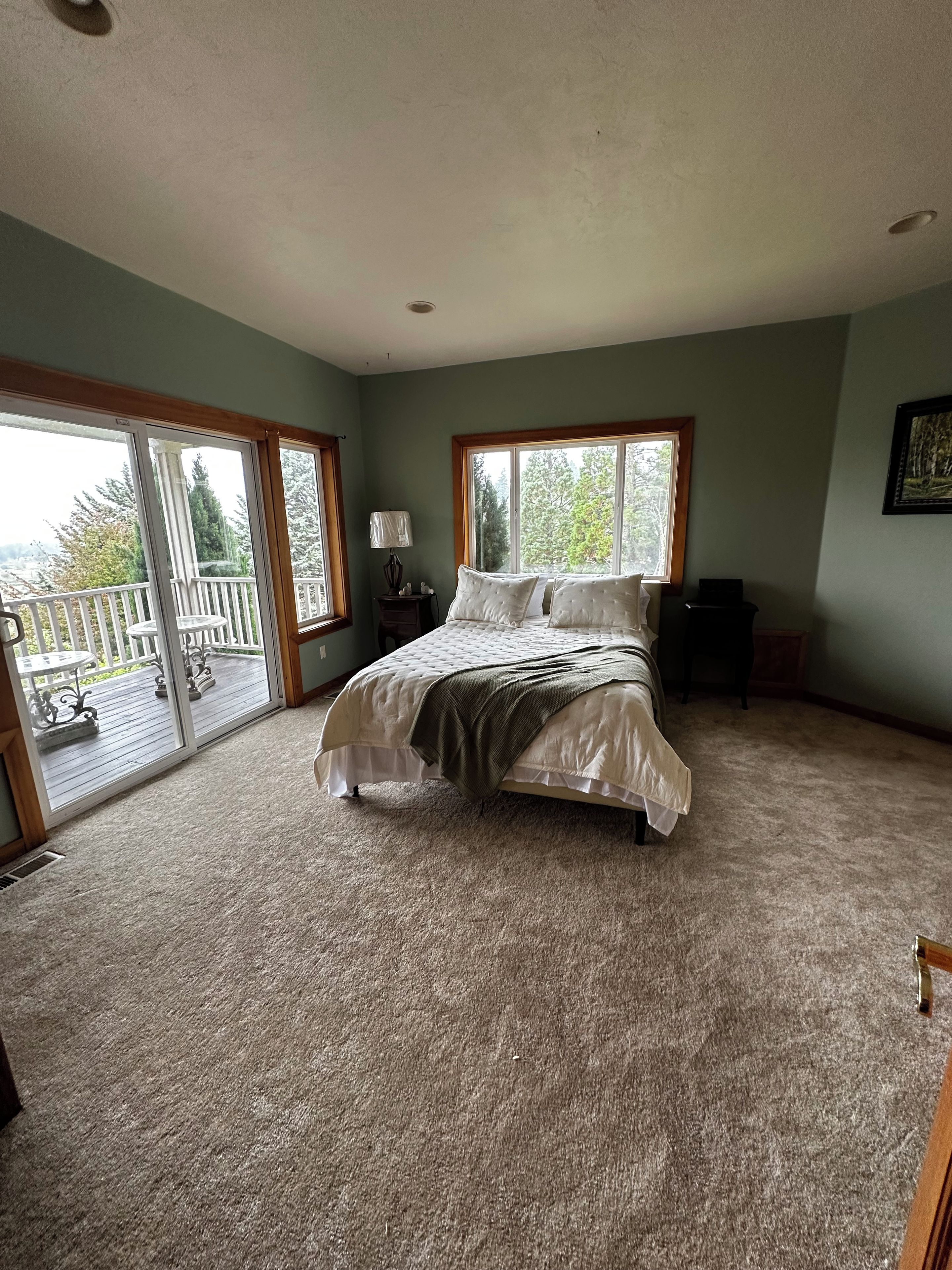 A bedroom with a large bed, a nightstand, a lamp, and a view of a deck through a sliding glass door.