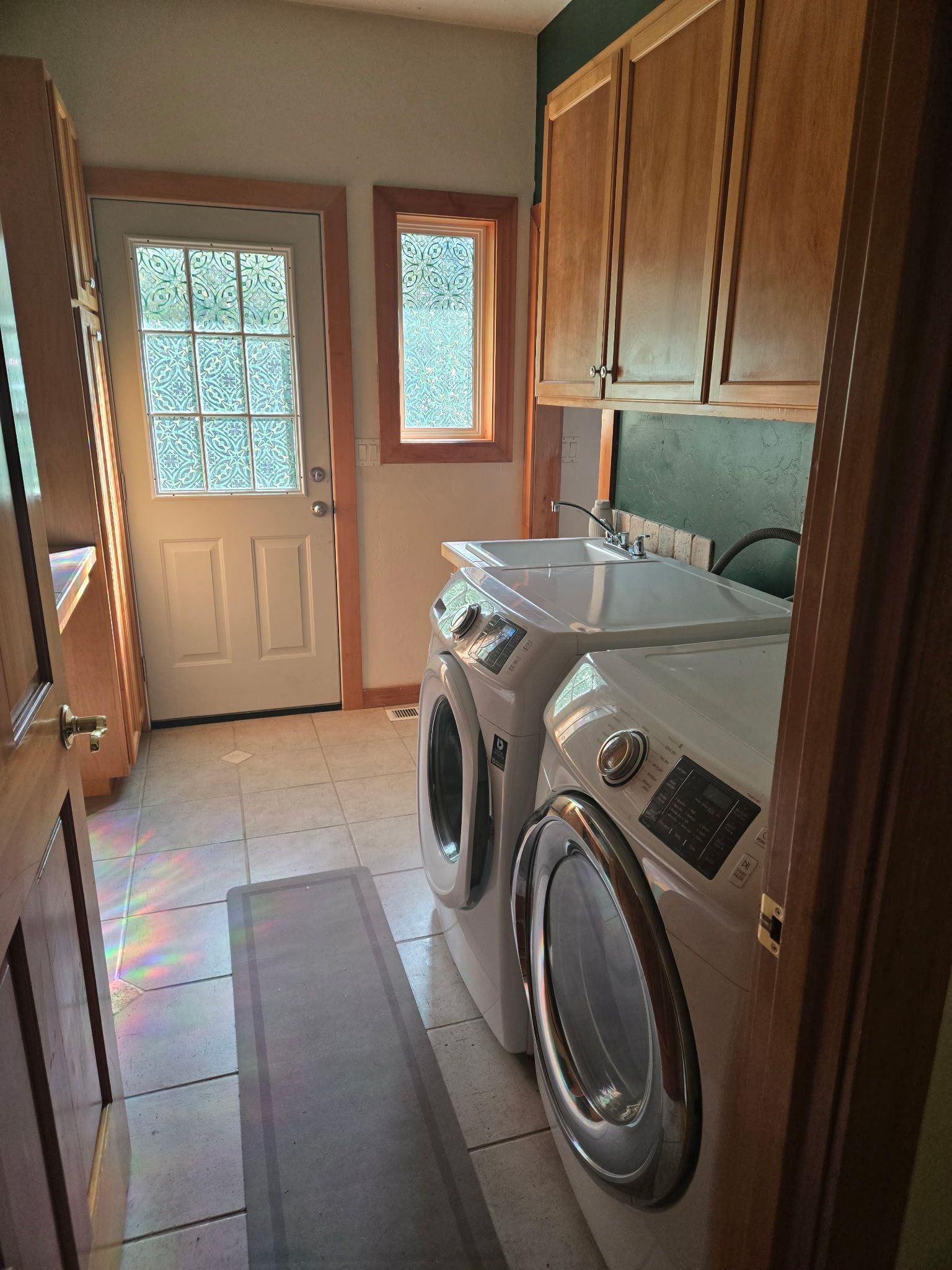 A laundry room with two front-loading washing machines, a dryer, wooden cabinets, and a door with a window.