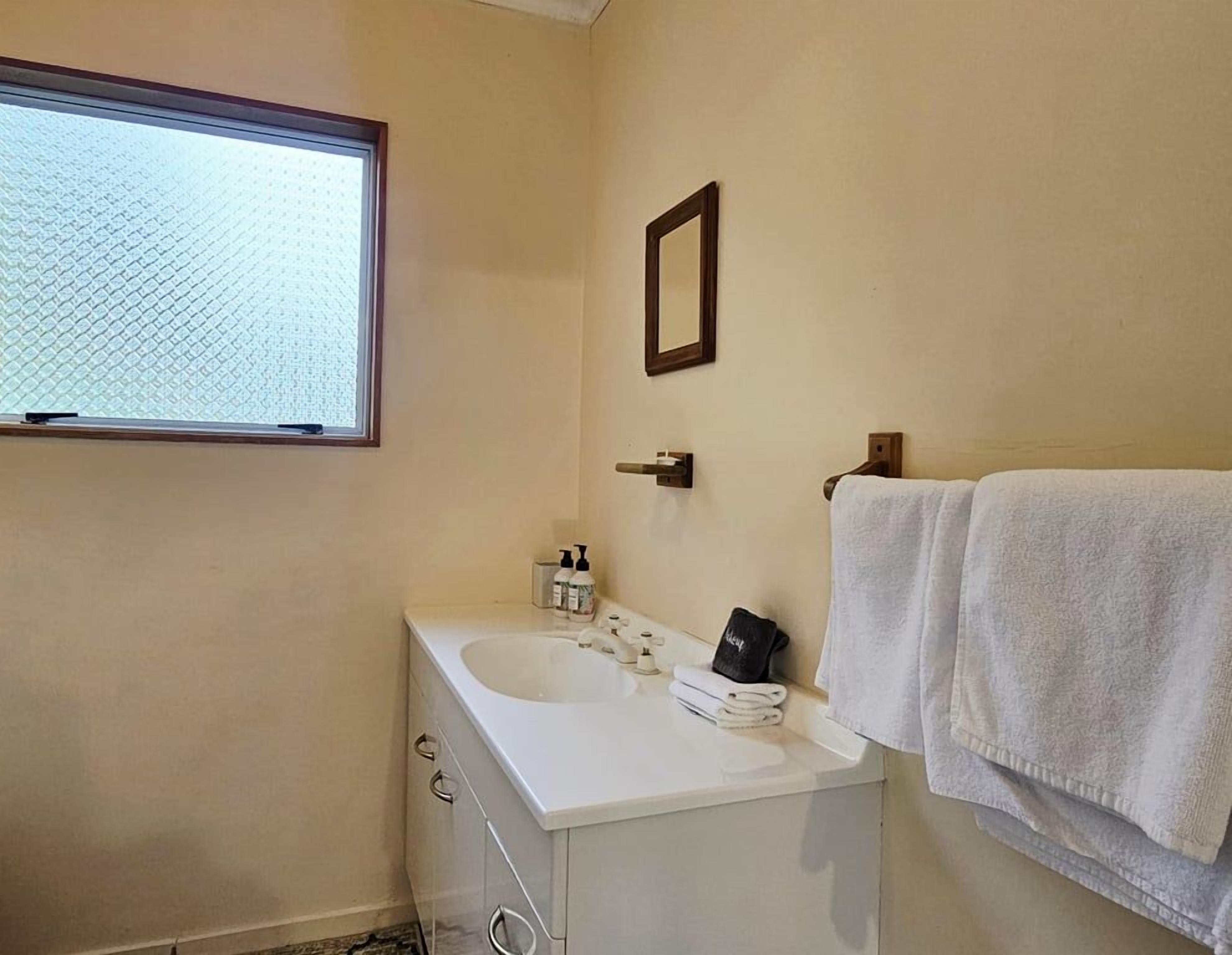 Un baño con ventana, lavamanos, espejo y toallero.