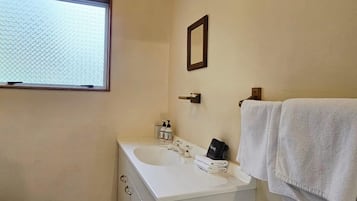 Un baño con ventana, lavamanos, espejo y toallero.