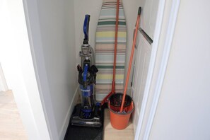 A narrow hallway with a vacuum cleaner, a striped bath mat, and a mop bucket. - Downtown 1BR | Gym + Coworking Area + Balcony (Kitchener)