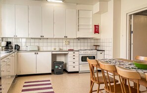 Une cuisine compacte avec des meubles blancs, une cuisinière, un évier et un coin repas comprenant une table et des chaises.