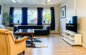 A living room with a sofa, a coffee table, a television on a stand, and a window with curtains. - 7 bedroom stunning home in östra ljungby (Östra Ljungby)