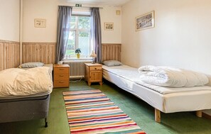 Ein Zimmer mit zwei Einzelbetten, einem Holzschrank, einem Heizkörper und einem Fenster mit Vorhängen.