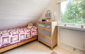 A bedroom with a sloped ceiling, a bed with a patterned bedspread, a dresser with drawers, a bedside table with a clock, and a window with a view of trees. - 4 bedroom gorgeous home in örkelljunga (Örkelljunga)