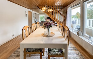 A dining area with a long table, wooden chairs, a vase with flowers, and a view of the outdoors through large windows. - 4 bedroom gorgeous home in örkelljunga (Örkelljunga)