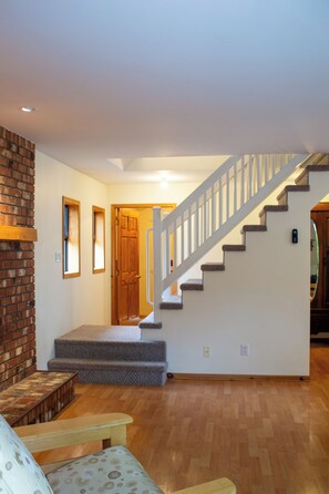 A staircase leading to an upper floor, a wooden bench, and a door in a room with wooden flooring.