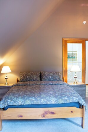 A bedroom with a wooden bed, patterned bedding, two bedside lamps, and a view through a door.