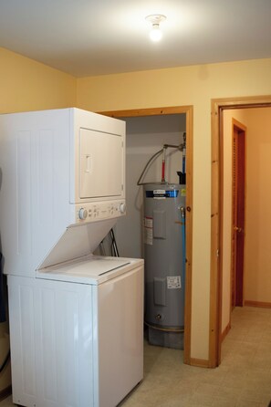 A laundry room with a front-loading washer and dryer, a water heater, and a door leading to another room.