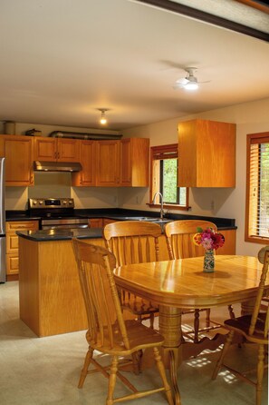 A kitchen with wooden cabinets, a stainless steel refrigerator, a built-in oven, and a dining area with a wooden table and chairs.