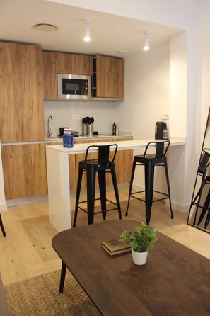 A modern kitchen with wooden cabinets, a microwave, and a coffee maker. There is a dining area with a table and chairs. - w* | Bright 1BR with Balcony in Central Madrid (Madrid)