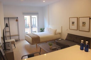 A hotel room with a bed, a sofa, a desk, a chair, a plant, and two framed pictures on the wall. - w* | Bright 1BR with Balcony in Central Madrid (Madrid)