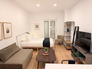 Ein modernes Schlafzimmer mit Bett, Sofa, Fernseher und Bücherregal.