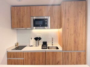 A modern kitchen with wooden cabinets, a stainless steel microwave, a coffee maker, and a sink. - w* | Lovely 1BR w/ Balcony in Central Madrid (Madrid)