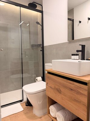 A modern bathroom with a glass-enclosed shower, a white toilet, and a wooden vanity with a sink. - w* | Lovely 1BR w/ Balcony in Central Madrid (Madrid)