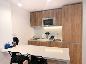 Une cuisine moderne avec des meubles en bois, un four à micro-ondes en acier inoxydable, un évier et un plan de travail blanc.