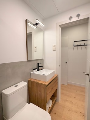 A modern bathroom with a white toilet, a wooden vanity with a sink, and a mirror above. - w* | Pleasant 1BR w/ Balcony in Central Madrid (Madrid)
