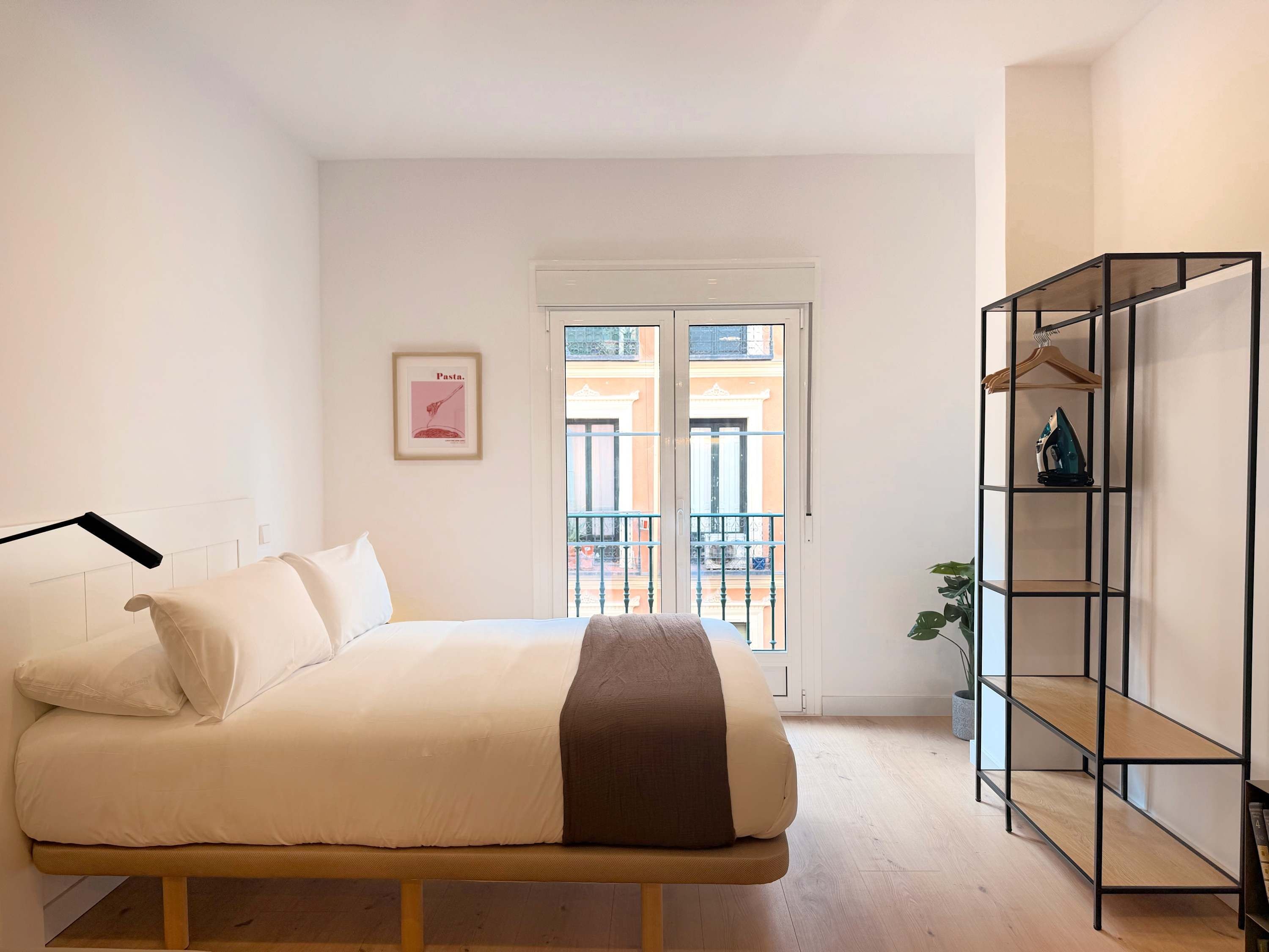 Ein Schlafzimmer mit einem Bett, einer Tür, die zu einem Balkon führt, und einer schwarzen Metallregaleinheit.