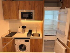 A compact kitchen with a built-in microwave, a washing machine, and a refrigerator with multiple shelves. - w* | Airy 1BR w/ Balcony in Central Madrid (Madrid)