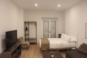 A bedroom with a bed, a TV, a chair, a small table with a plant, and a wardrobe. - w* | Charming 1BR with Balcony in Central Madrid (Madrid)