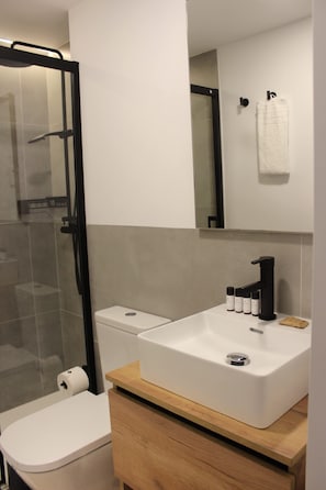A modern bathroom with a white toilet, a white sink with black faucet, and a glass shower enclosure. - w* | Charming 1BR with Balcony in Central Madrid (Madrid)