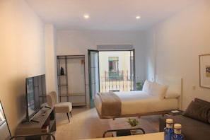 A hotel room with a bed, a desk, a chair, a TV, and a balcony. - w* | Charming 1BR with Balcony in Central Madrid (Madrid)