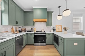 A kitchen with green cabinets, a stainless steel oven, and a white countertop. - Music City Home Base | Office + 98" TV | 30+ Days (Nashville)