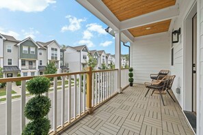 A covered balcony with a wooden floor, white railing, and a seating area with two chairs. - Music City Home Base | Office + 98" TV | 30+ Days (Nashville)