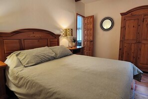 A bedroom with a wooden headboard, a bed with a light-colored bedspread, a bedside lamp, a mirror, and wooden wardrobes. - Casa Frida - Beach City retreat (Ensenada)