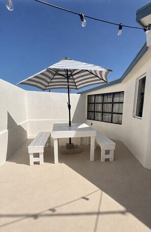 A patio with a table and benches, an umbrella, and string lights. - Casa Frida - Beach City retreat (Ensenada)