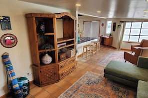 A living room with a wooden cabinet, a green sofa, a patterned rug, and a window with curtains. - Casa Frida - Beach City retreat (Ensenada)