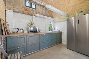 Een keuken met een houten aanrecht, een ingebouwde magnetron, een roestvrijstalen koelkast en een raam met uitzicht op groen.