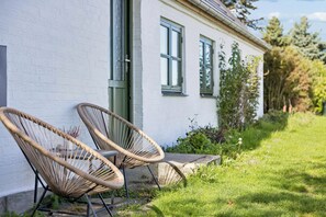 Een wit gebouw met twee rieten stoelen buiten, een groene deur en een raam met luiken.