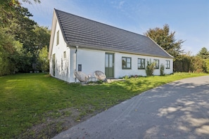 Een laag wit huis met een grijs dak, een geplaveid pad en een gazon.