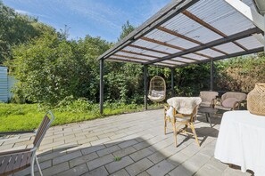 A covered patio area with outdoor furniture, including a table and chairs, and a hanging chair. - Charming holiday home on Northern Langeland (Tressebølle)