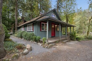 Ein rustikales Blockhaus mit Veranda, umgeben von Bäumen und einem Schotterweg.