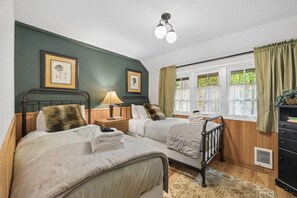 Ein Zimmer mit zwei Betten, einem Nachttisch mit Lampe, einem Schminktisch und einem Fenster mit Vorhängen.