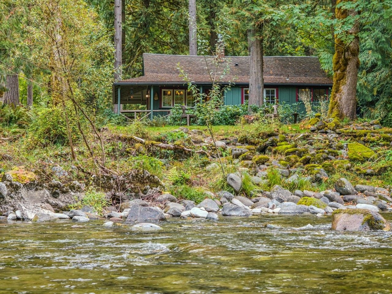 A cabin by a river surrounded by trees.